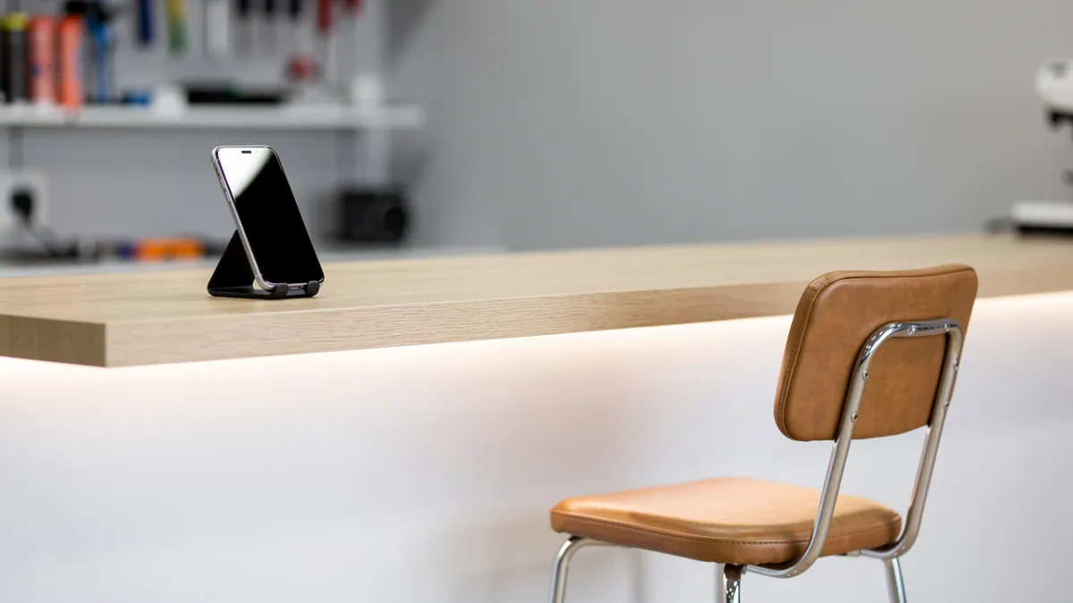 Técnico de assistência de celular atendendo um cliente na bancada e mostrando a peça trocada